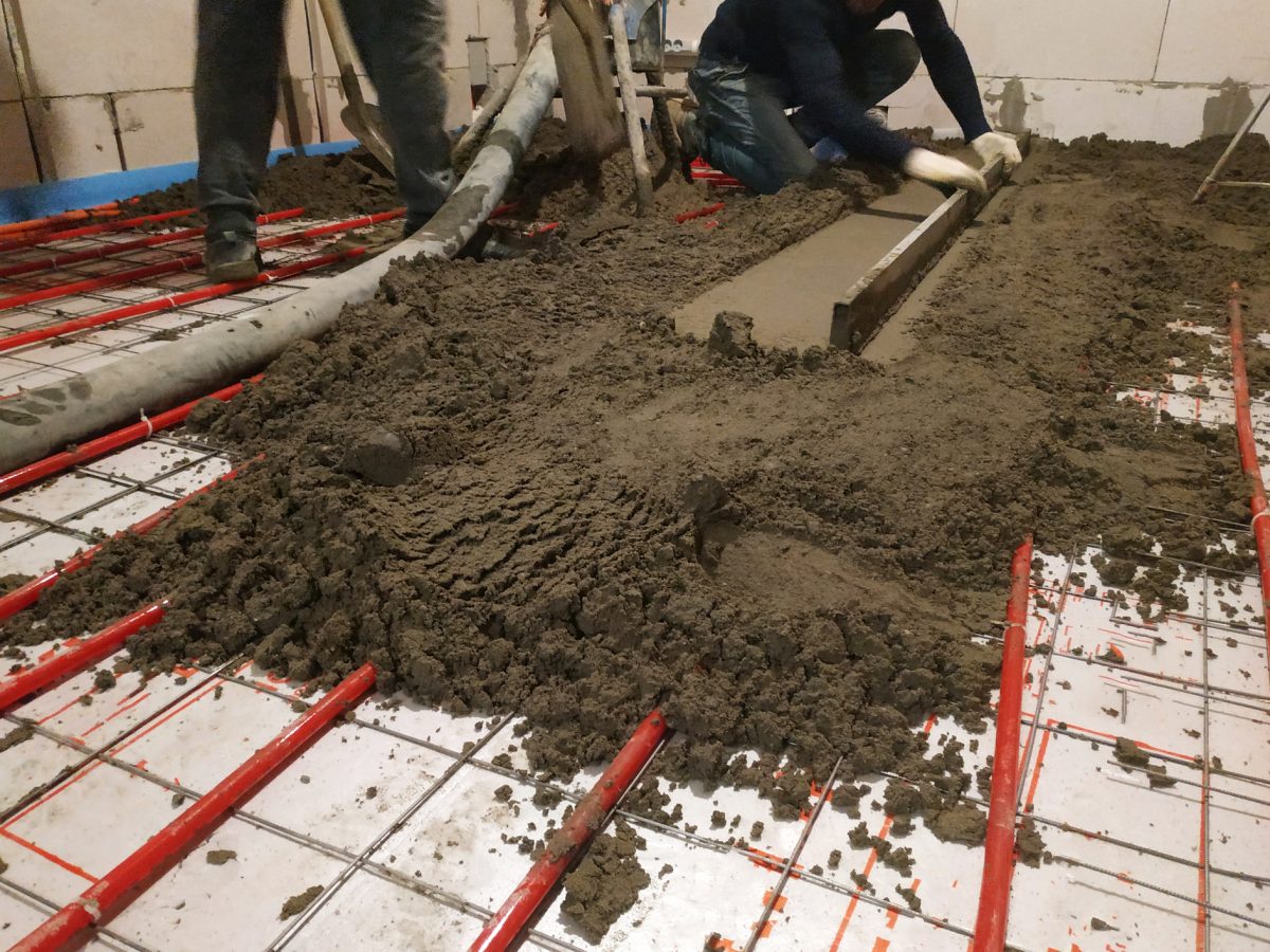 In the newly built house the worker performs a sand-cement screed for heating.
